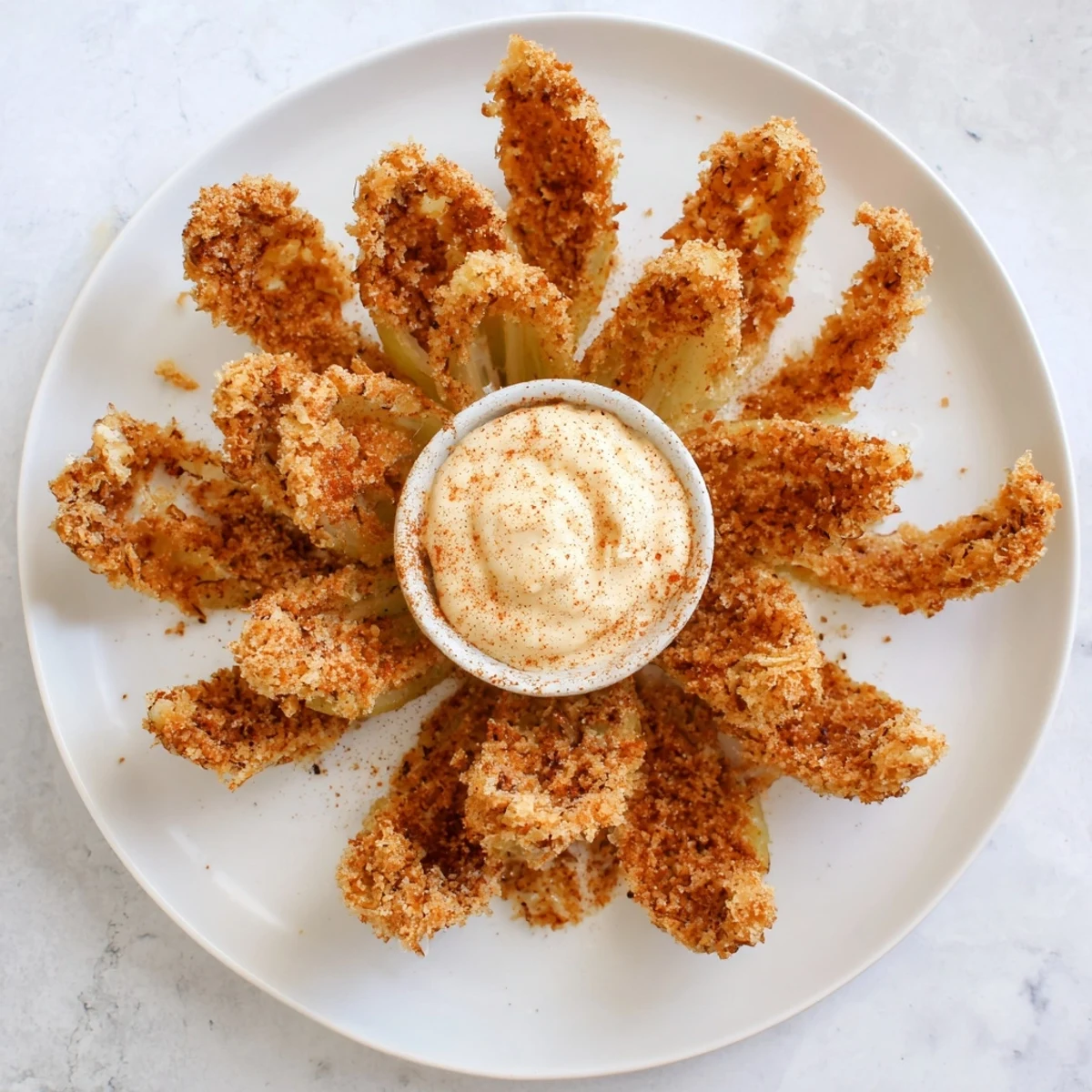 A whole deep-fried Blooming Onion with crispy golden petals served with creamy red dipping sauce.