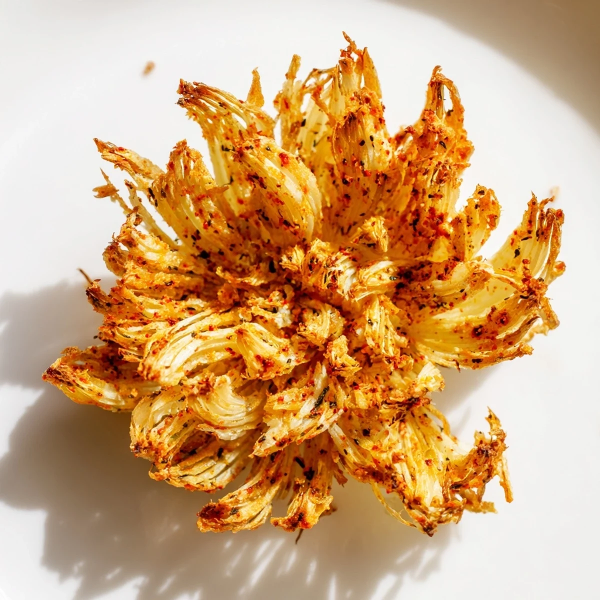 Crisp, battered Onion Petals stacked on a plate next to a small bowl of spicy dipping sauce for easy sharing.