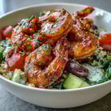 A vibrant Mediterranean Shrimp Bowl featuring pink shrimp, tomatoes, cucumbers, and olives, finished with lemon wedges.