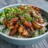Asian Shrimp Bowl served in a ceramic bowl, garnished with scallions and julienned carrots, showcasing colorful vegetables and glistening dressing on warm jasmine rice.