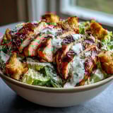 A freshly tossed Caesar Chicken Bowl drizzled with creamy Caesar dressing, ready to serve for a light dinner.