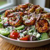 Grilled Greek Shrimp Bowl with charred shrimp, feta, cucumbers, tomatoes, and olives on a bed of greens.