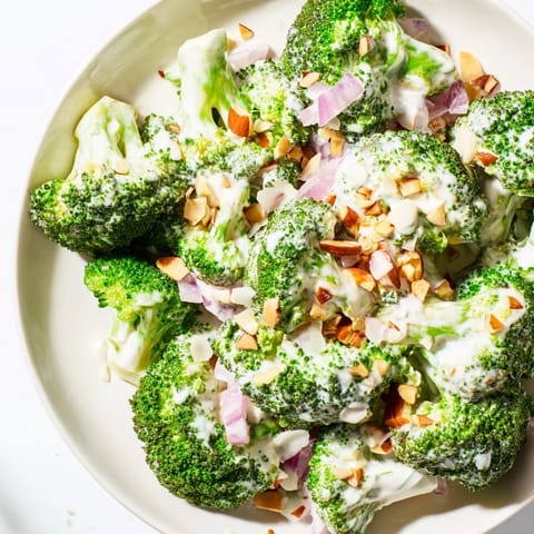 Fresh Garlic Parmesan Broccoli Salad in a white bowl, topped with sliced red onion and halved cherry tomatoes for a vibrant lunch.