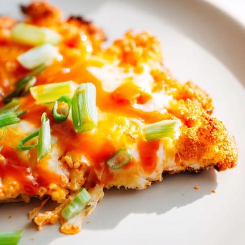 Freshly baked Buffalo Cauliflower Pizza slice with melted cheese and tangy buffalo drizzle on a rustic board.  