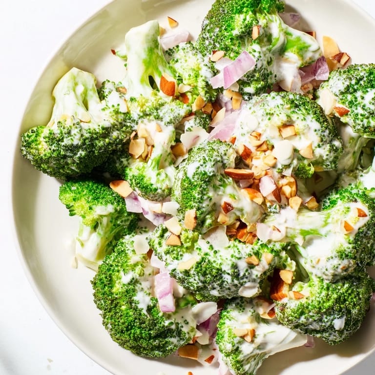 Fresh Garlic Parmesan Broccoli Salad in a white bowl, topped with sliced red onion and halved cherry tomatoes for a vibrant lunch.
